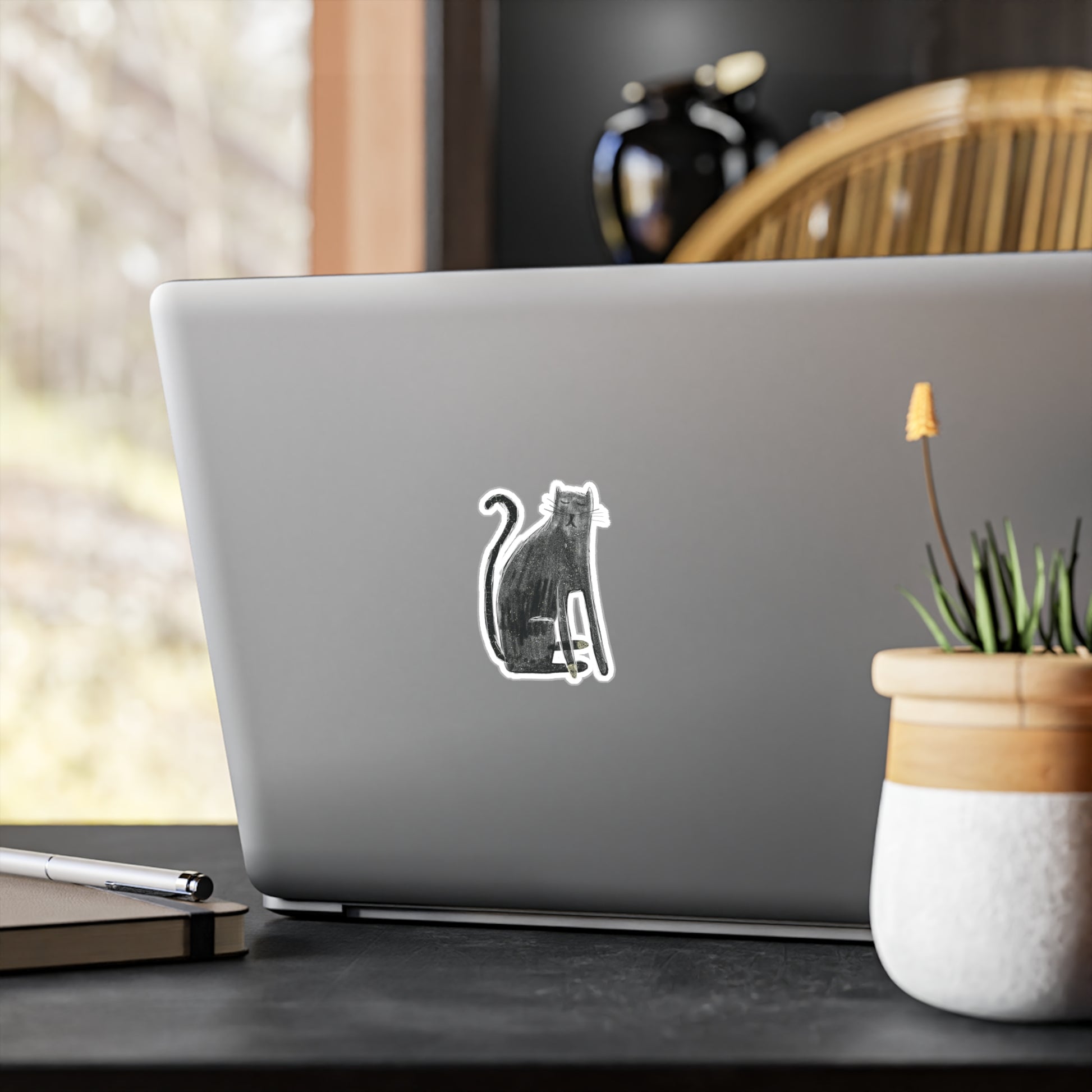 Laptop with a cat sticker on a desk with a plant and pen