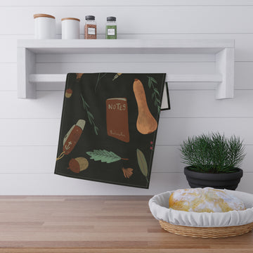 Black towel with autumnal design hanging on a wooden shelf with a plant and basket below.