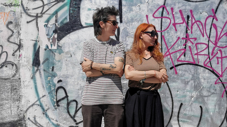 Two people standing in front of a graffiti-covered wall.