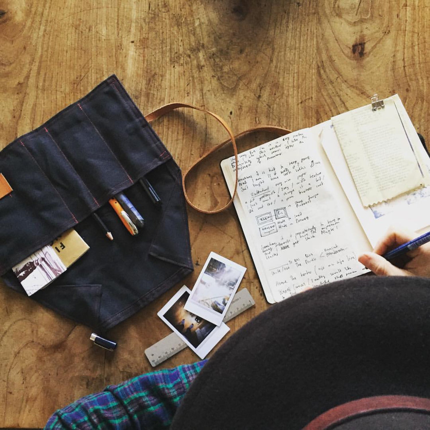Person writing in a notebook with a pen holder and photos on a wooden table