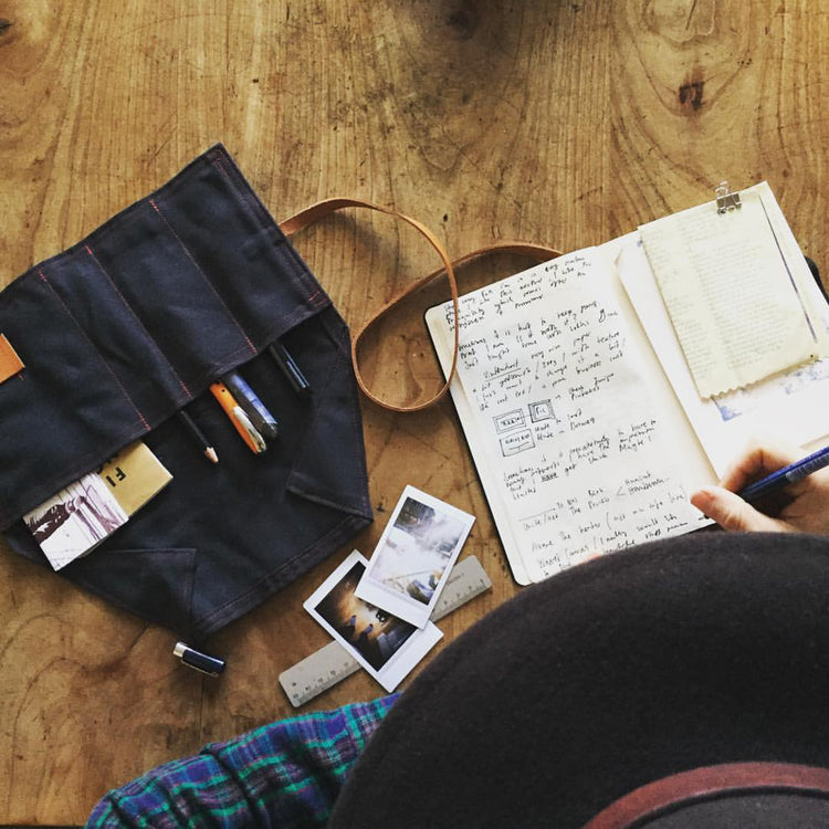 Person writing in a notebook with a pen holder and photos on a wooden table